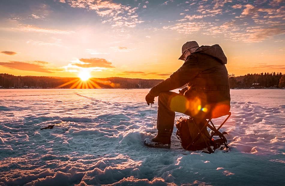 Man ice-fishing at sunset during winter in Lapland, Finland