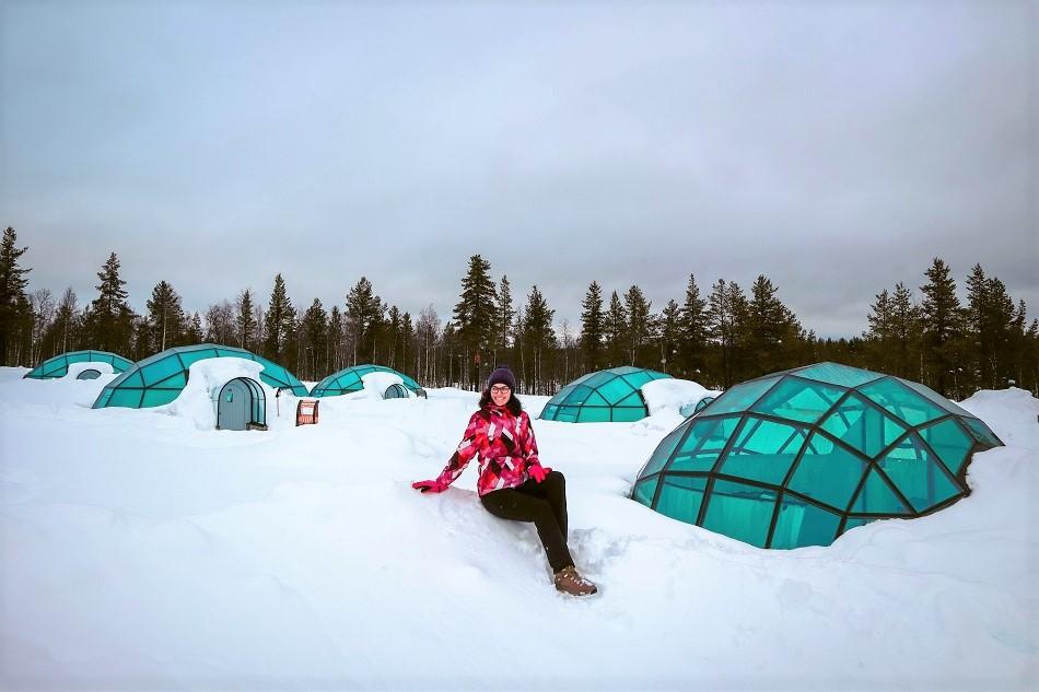 Girl sitting in front of glass igloo village in Lapland in winter at Kakslauttanen Arctic Resort Lapland