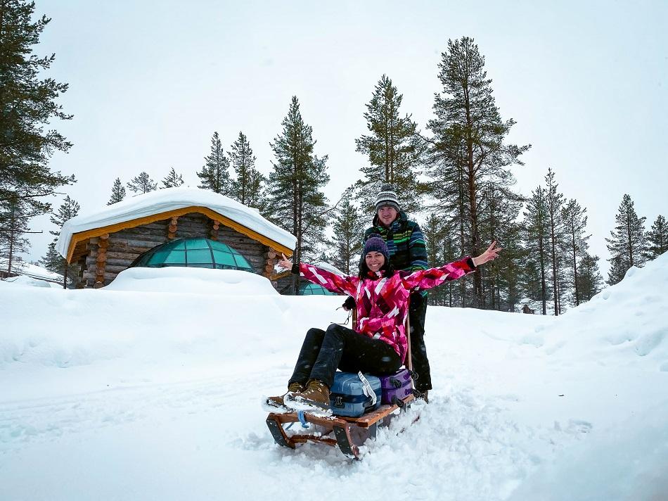 Aurelia Teslaru and Dan Moldovan sitting in front of Kelo Glass Igloo on a sled at Kakslauttanen Arctic Resort Lapland during winter