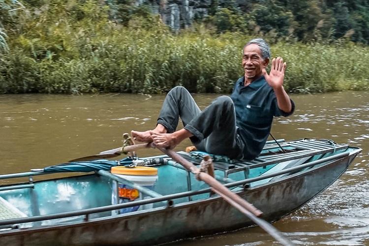 Vietnamese man waving his hand while rowing the boat with his feet in Tam Coc, Ninh Binh